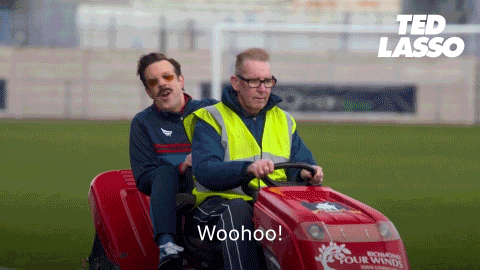 Gif of the TV show character Ted Lasso riding pillion in a football cart and celebrates as he shouts "Woohoo" with his left hand moving up and down in the air 