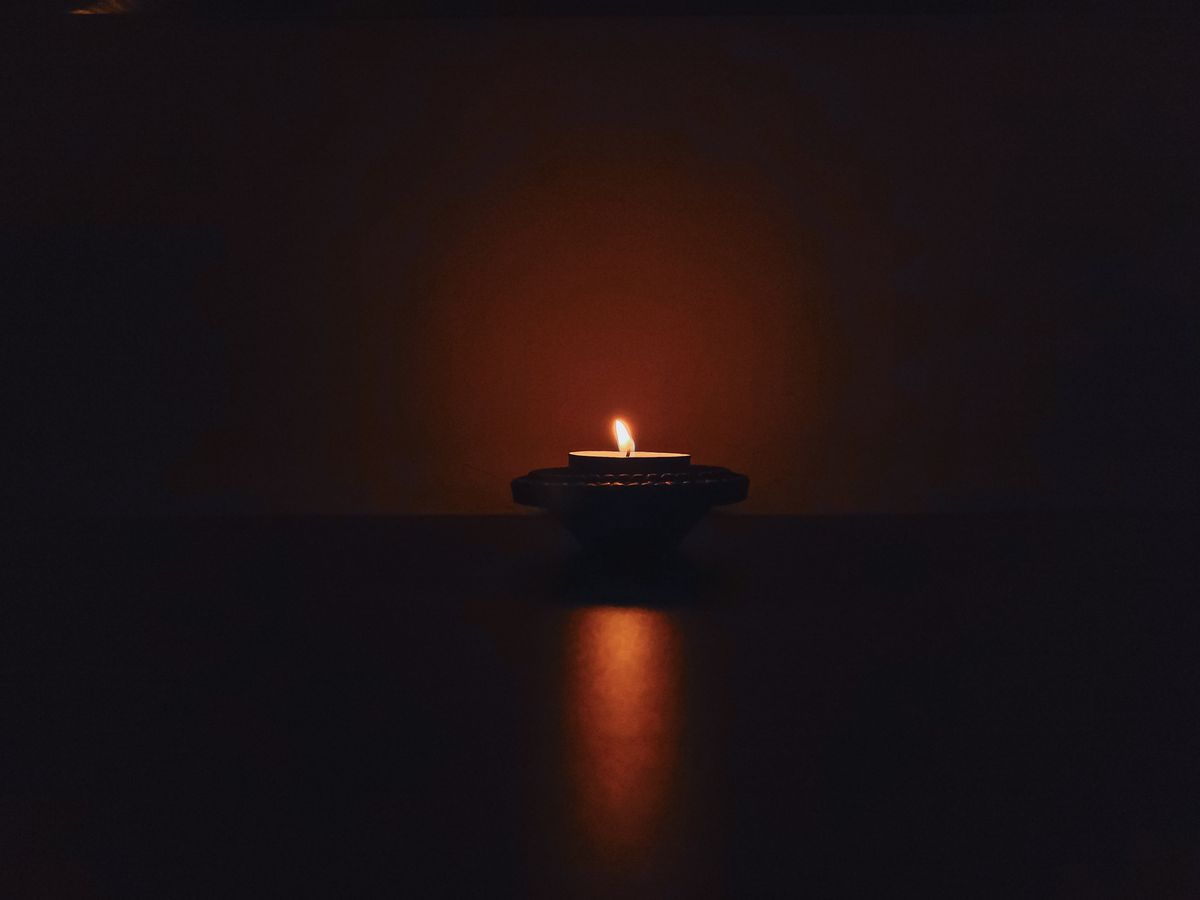 A floating candle on a diya illuminates a dark room. The reflection falls on the opaque table in a fuzzy shape.